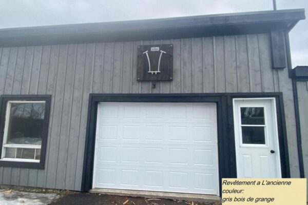 Façade grise avec garage et porte blanche.